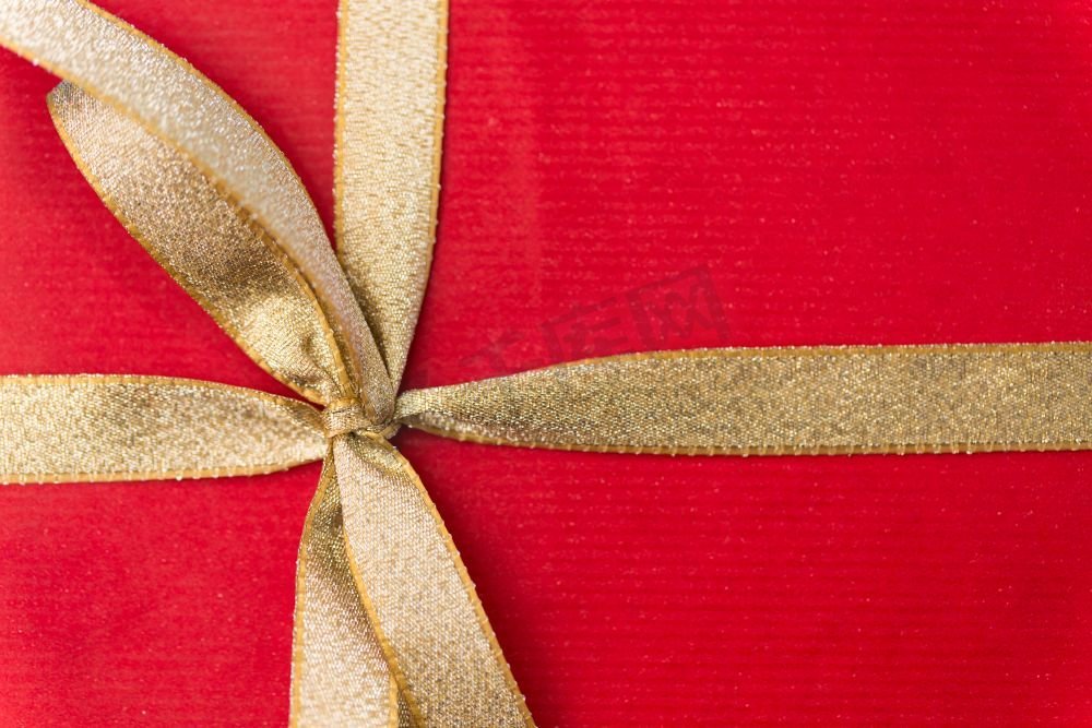 节日，问候和惊喜概念-金色蝴蝶结圣诞红色礼盒特写。圣诞红色金色蝴蝶结礼盒特写图片