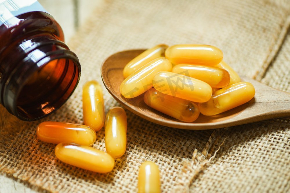 蜂王浆胶囊在木勺和袋子背景/黄色胶囊药物或补充食品从自然健康图片