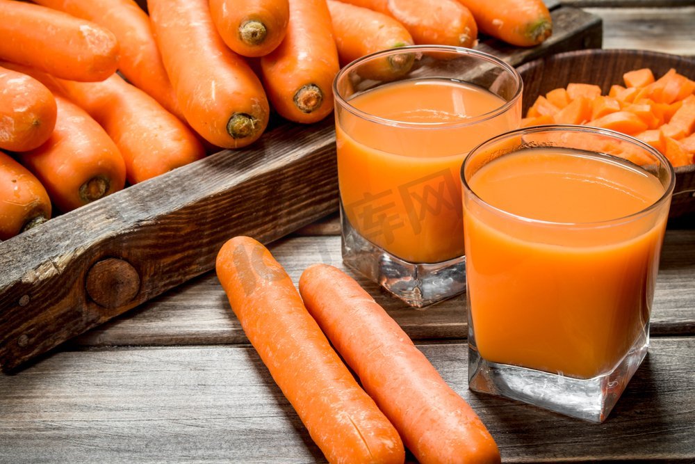 玻璃杯里的胡萝卜汁。在木制的背景上..玻璃杯里的胡萝卜汁。图片