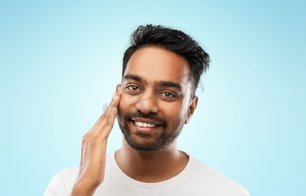 修饰，皮肤护理和人的概念—微笑的年轻印度人接触他的脸在蓝色背景微笑的印度人触摸他的脸图片