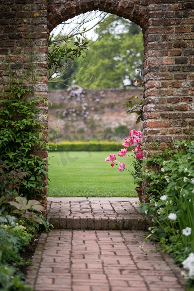 古英国乡村花园景观中的拱门，春天里种着郁金香和边境植物图片