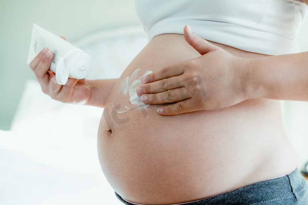 快乐的孕妇在孕妇肚子上涂抹护肤霜，防止妊娠纹。健康肌肤按摩护理及保湿护理理念。图片