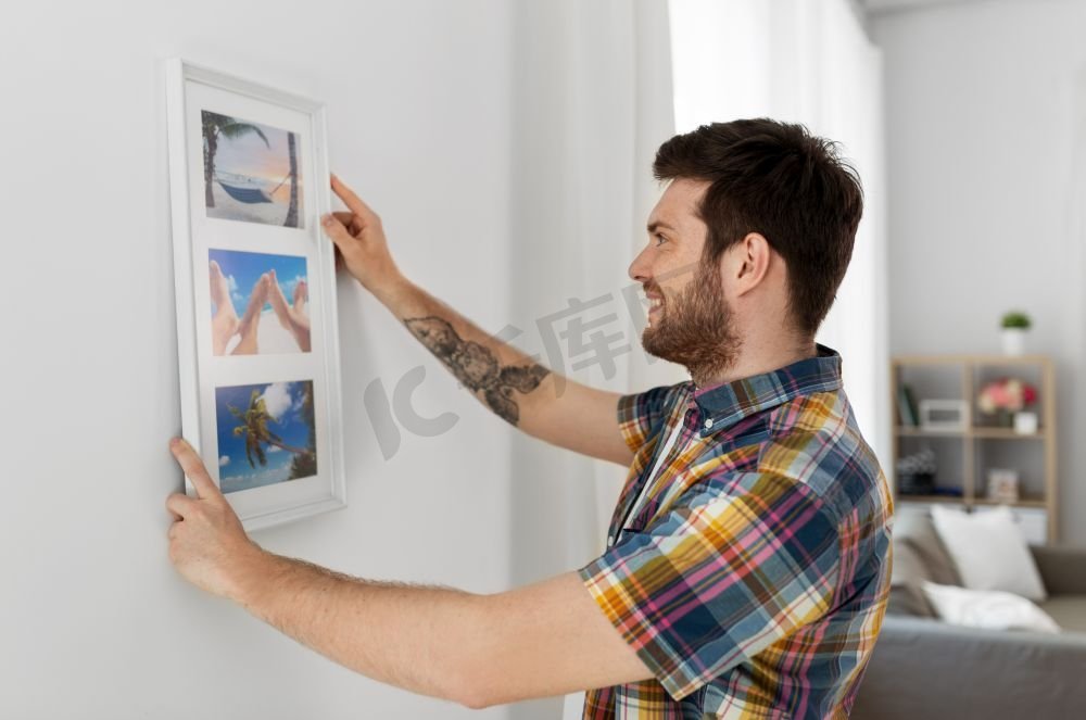室内装饰和装修概念—微笑的男子挂在框架的图片到墙上在家里。一个人在家里把画挂在相框里的墙上图片