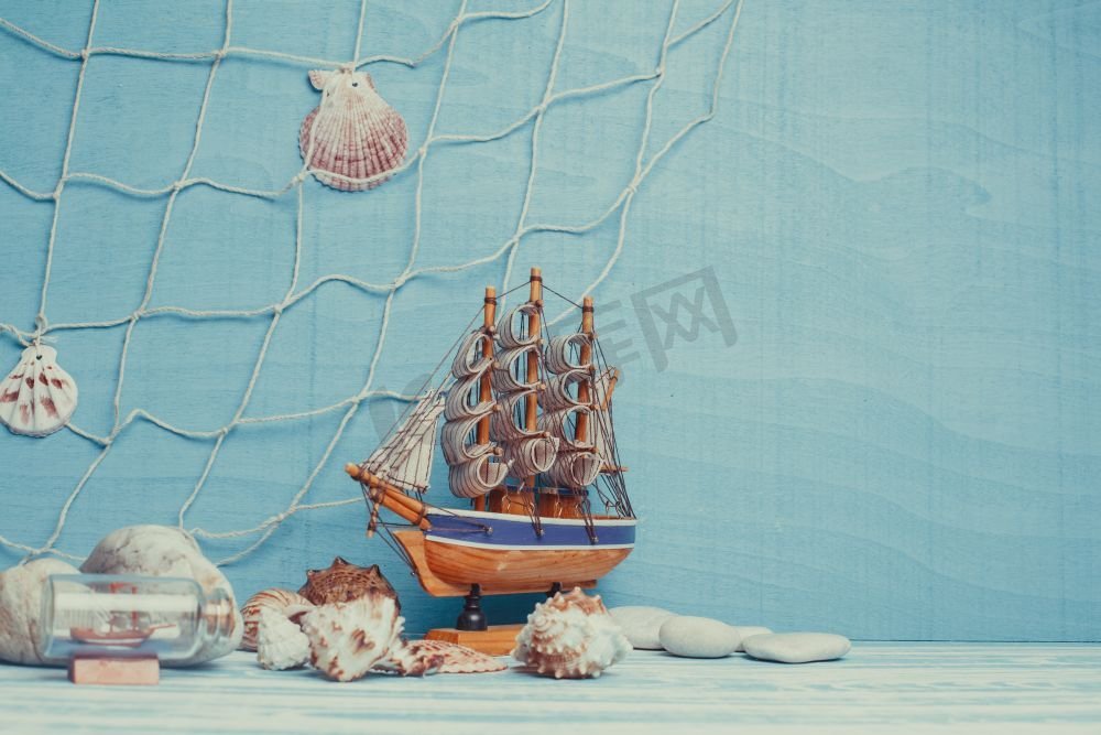 漂亮的海洋构图，蓝色背景上有玩具帆船、贝壳、玻璃瓶和渔网。海上室内装饰图片