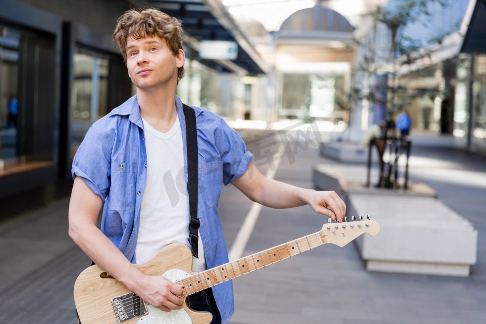 城市里弹吉他的年轻音乐家。城市里拿着吉他的年轻音乐家的肖像图片