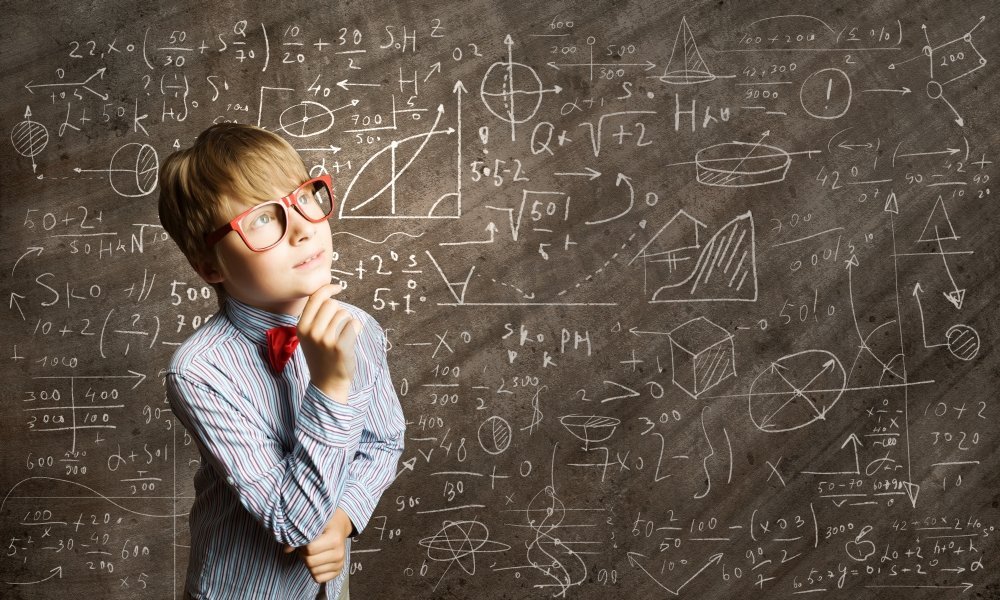 聪明的小学生。戴着红眼镜的天才男孩在黑板上写着公式图片