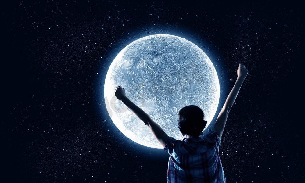 满月。举起双手仰望天空中月亮的年轻女子的背影图片