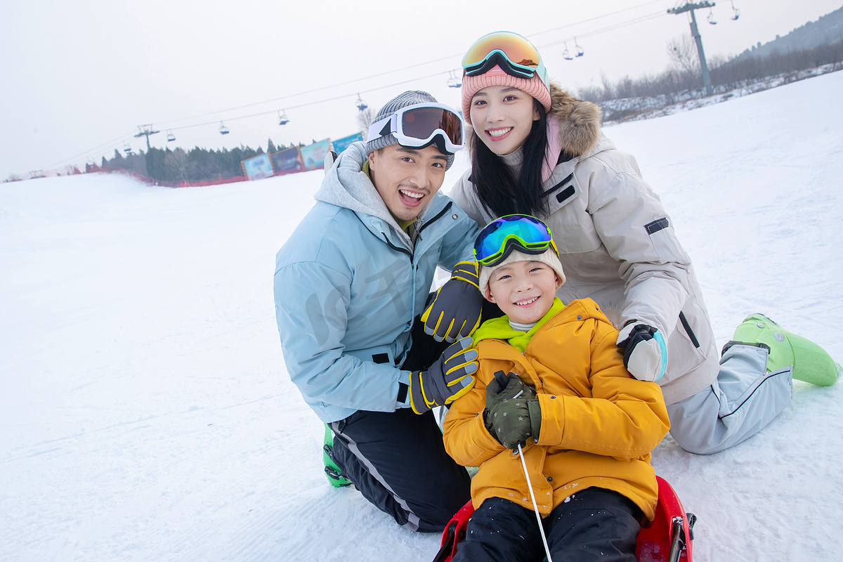 滑雪场上父母和坐在雪上滑板的儿子图片