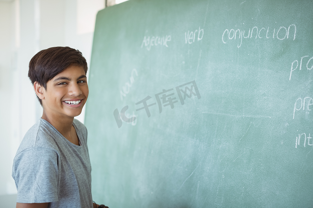 微笑的小学生站在教室黑板附近的肖像图片