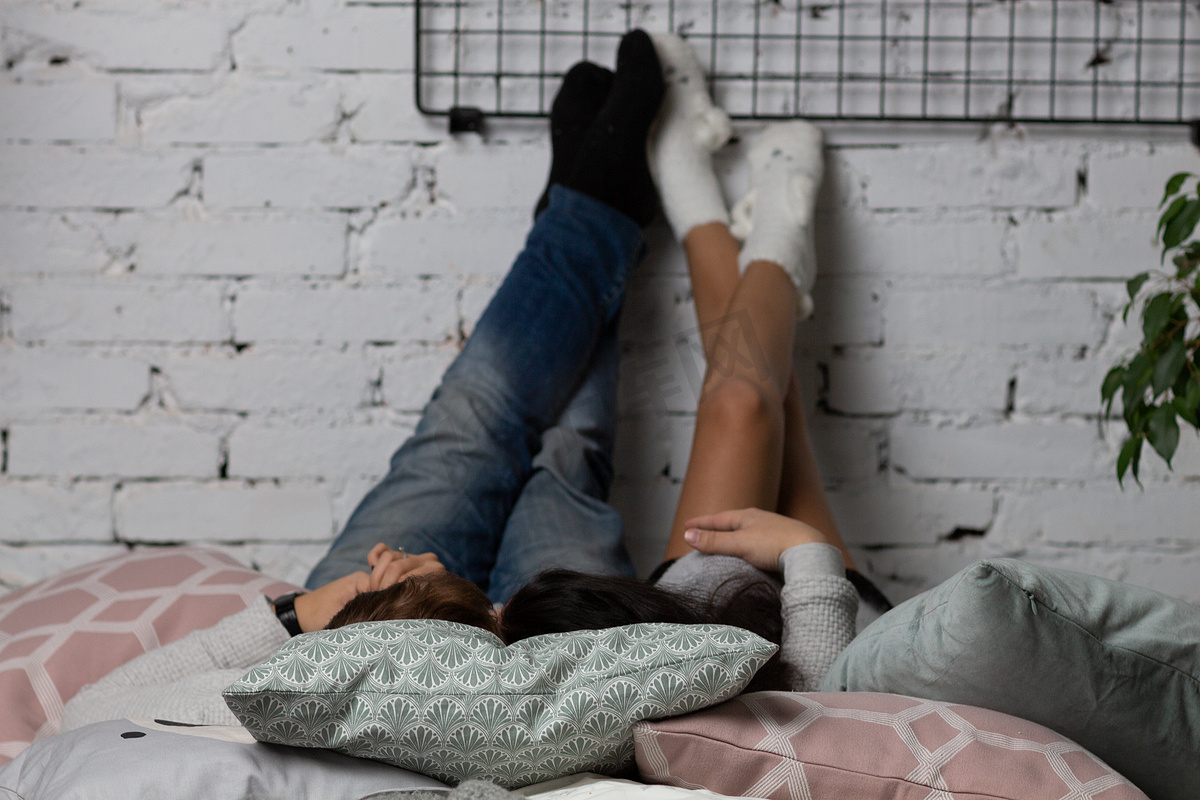 一个年轻人和他的女朋友躺在床上，把脚扔在白砖墙上图片