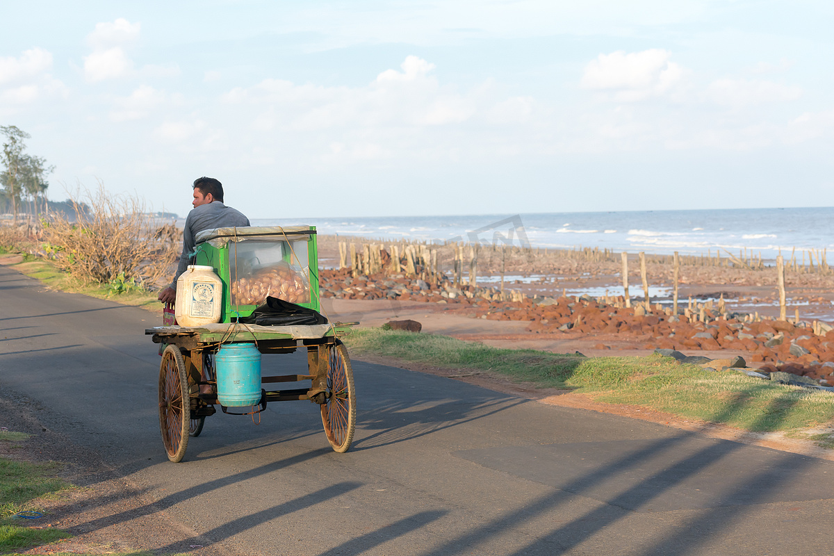 夏日夕阳下，在沿海地区海滩路上，一个农村流动街头食品卖家在传统的人力车上销售 phuchka、gol gappa、chaat 和 pani puri。图片