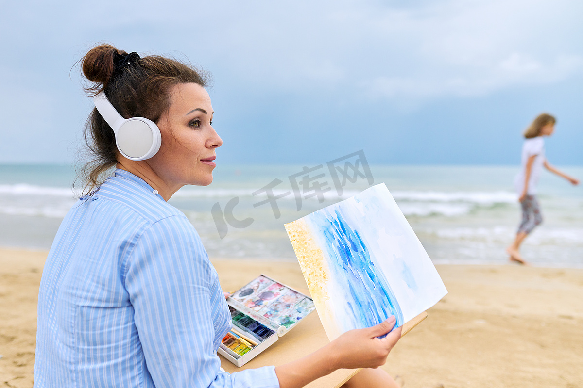 戴着耳机听音乐享受水彩画的成熟女性图片