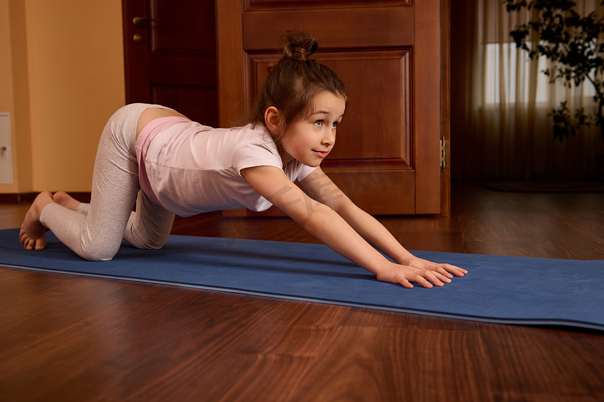 运动型女童在健身垫上伸展身体和背部、练习瑜伽、在室内锻炼的侧面肖像图片