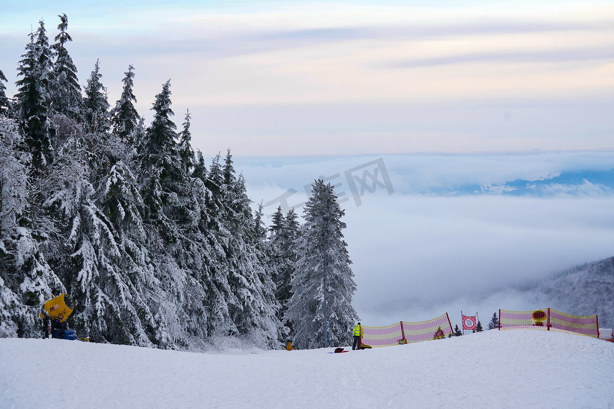 在德国 Hessen Rhoen 的 Wasserkuppe 山脉和天空的背景下，在云杉林中有滑雪场和滑雪缆车的冬季山脉全景。图片