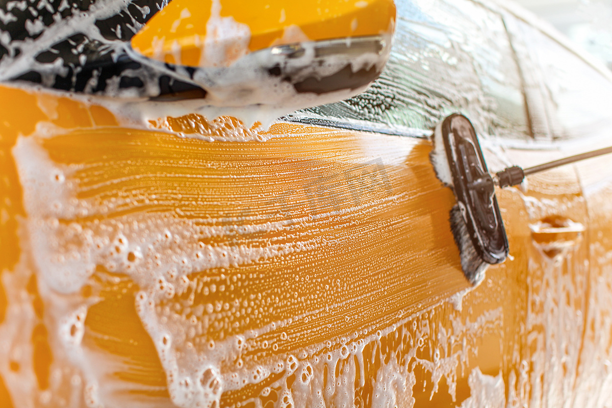 在自助洗车场洗车的一侧，黄色油漆上可见白色洗发水刷子的笔触。图片