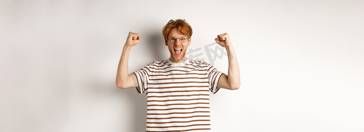 快乐的红头发人像赢家一样举起手来，获奖庆祝，欢呼雀跃，站在白色背景上图片