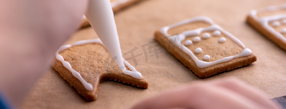 年轻女人正在家里装饰圣诞姜饼屋曲奇饼干，在糖衣袋里装上糖霜，特写，生活方式。图片