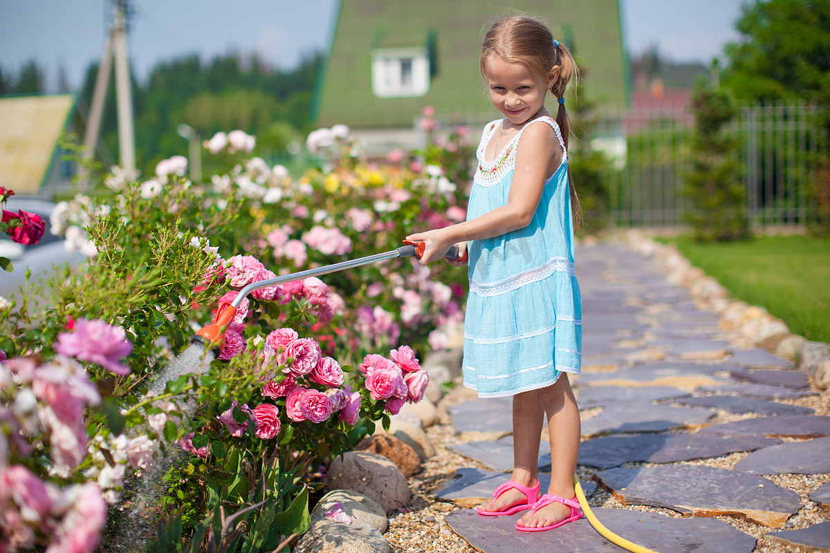 穿着蓝色裙子的可爱女孩在花园里用软管浇花图片