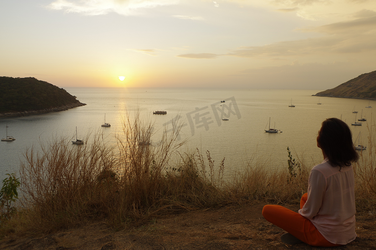 坐在瑜伽莲花冥想位置的年轻女孩坐在海边的岩石上，看着太阳在黄金时段落下。图片