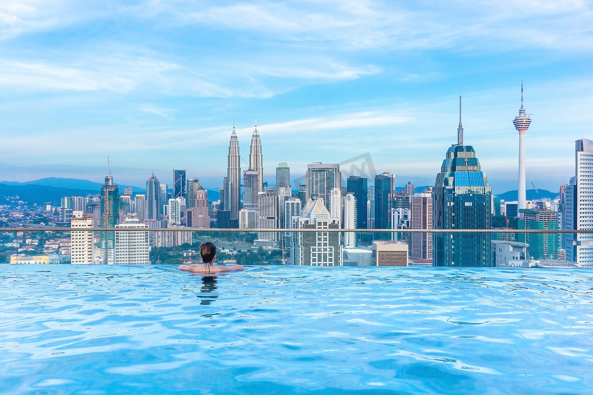 在无边泳池屋顶放松的女性，欣赏马来西亚吉隆坡美丽的城市摩天大楼景观图片