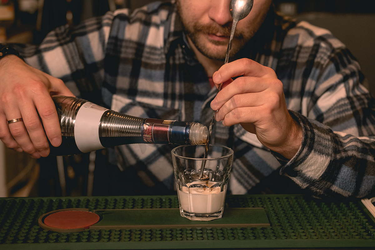 调酒师在准备鸡尾酒白俄罗斯时将咖啡利口酒倒入加奶油的玻璃杯中图片