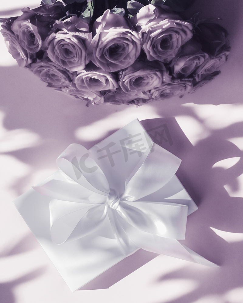 豪华假日丝绸礼盒和紫色背景的玫瑰花束、浪漫惊喜和鲜花作为生日或情人节礼物图片