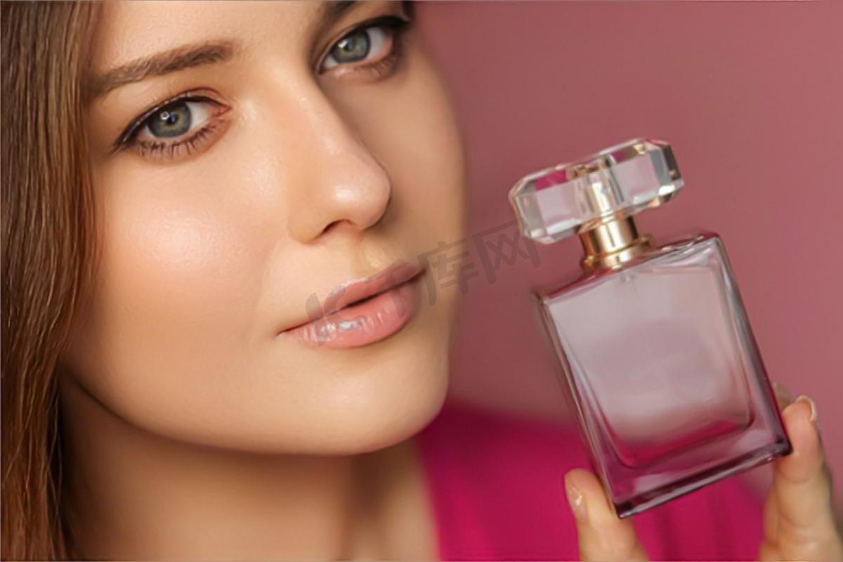 粉红色背景的香水、美容产品和化妆品模特脸部肖像，美丽的女人拿着带有花卉女性香味、时尚和化妆的香水瓶图片