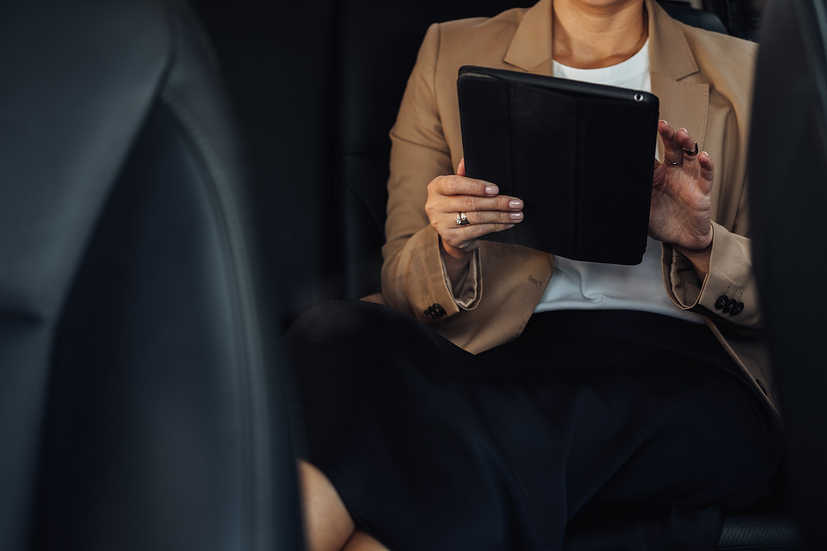 坐在汽车后座上使用平板电脑工作的难以辨认的女企业家图片