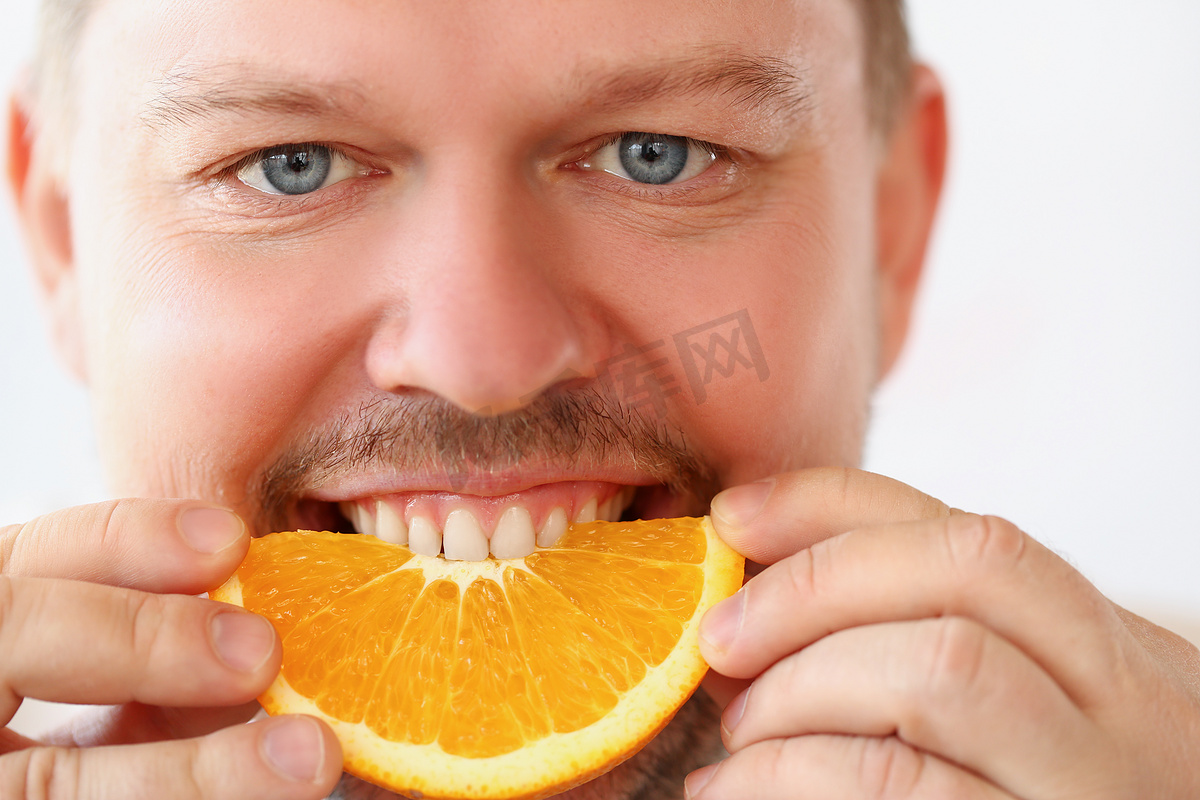 男人在厨房吃早餐时咬切碎的橙子片，健康饮食，严格饮食图片