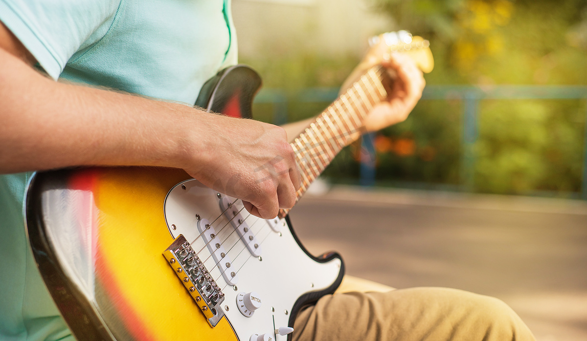 快乐的年轻人嬉皮士坐着弹吉他，特写，夏日阳光，户外图片
