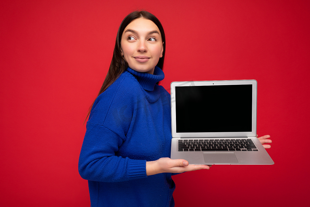 红墙背景上突显的深蓝色毛衣美女手持电脑笔记本电脑的肖像照片图片
