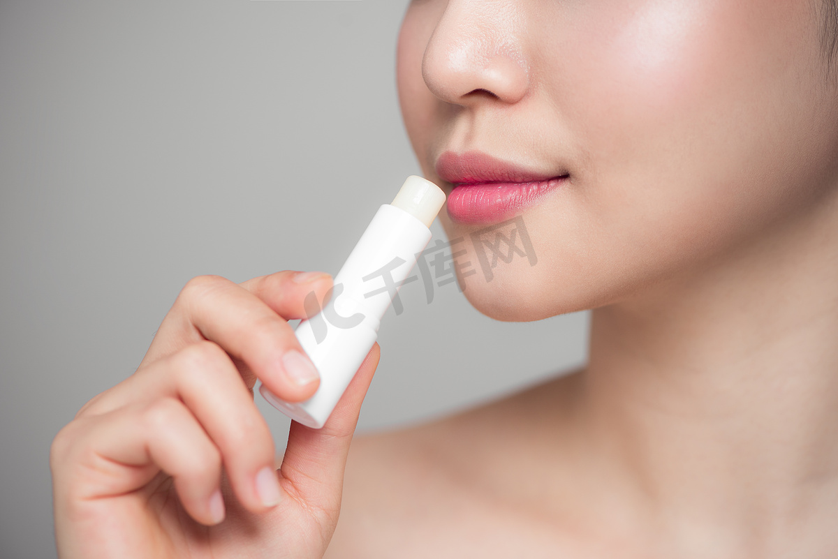 灰色背景下涂卫生润唇膏的亚洲女性图片