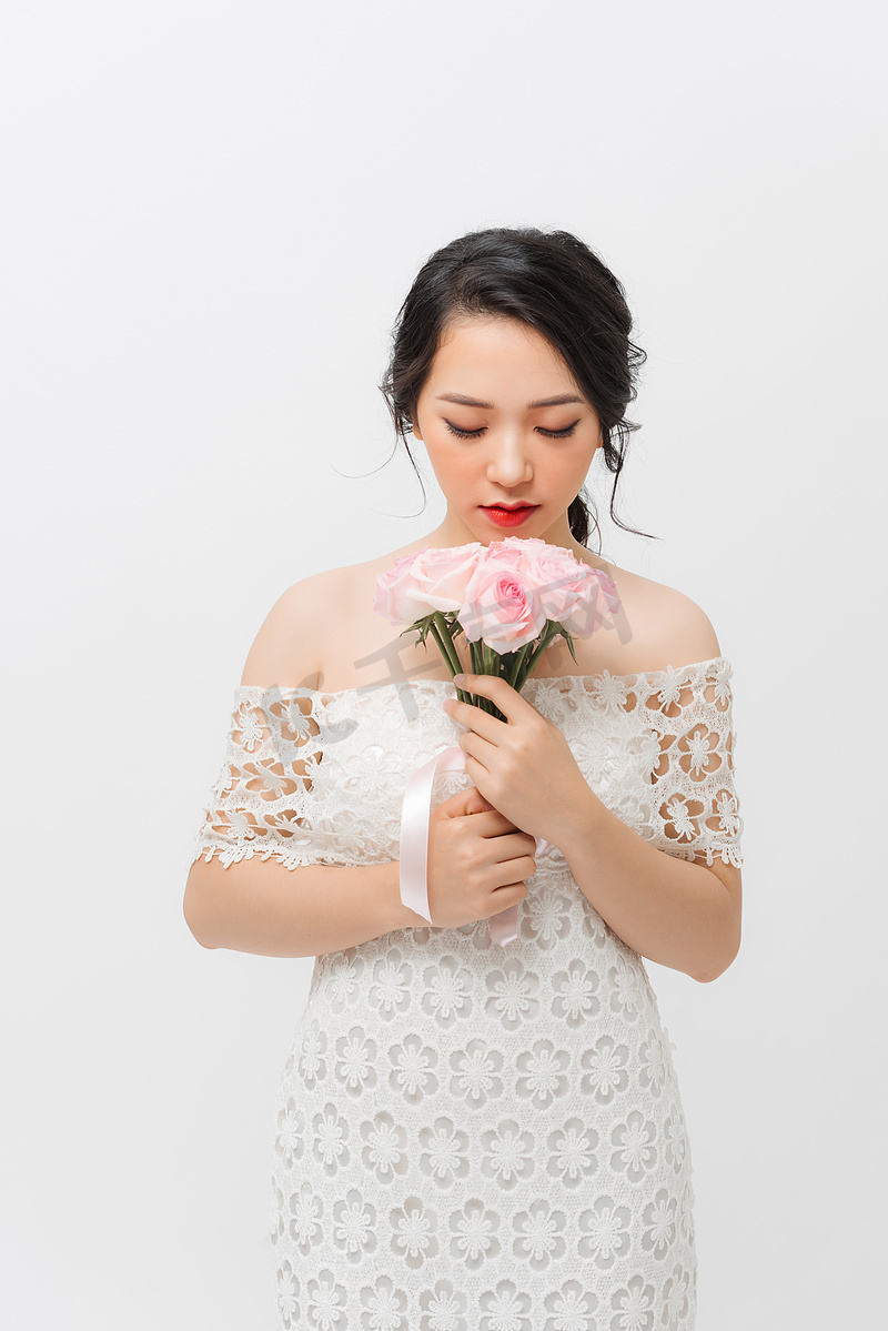 一个美丽的少妇嗅到桃红色玫瑰并且看下来的外形画象，隔绝在白色背景。图片