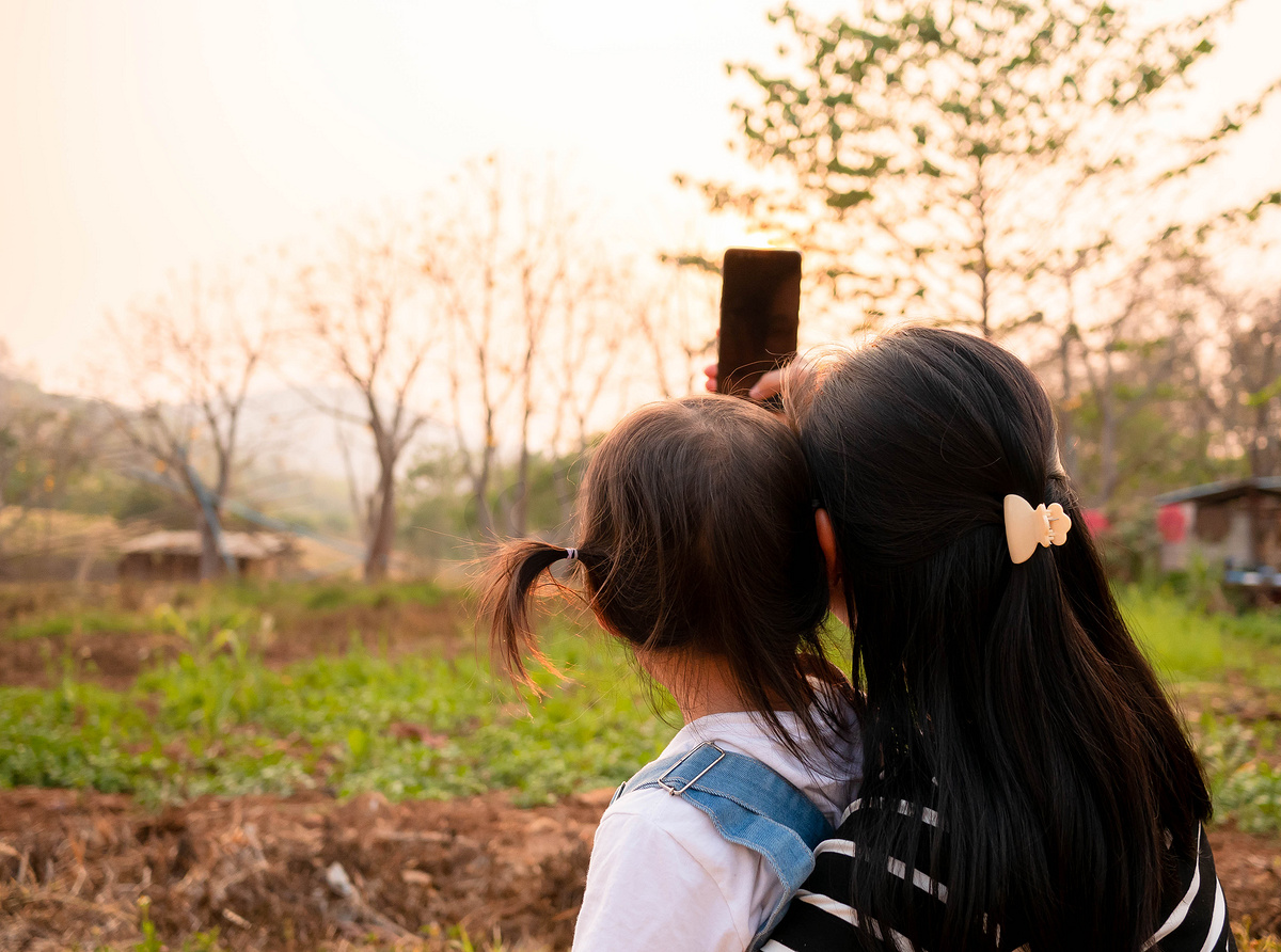 亚洲小女孩在日落背景下在花园里与母亲合影的后视图。图片