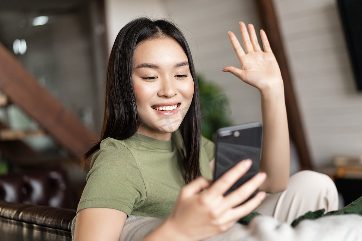 年轻的亚洲女性用手机视频通话，对着智能手机摄像头挥手，在家用手机聊天图片