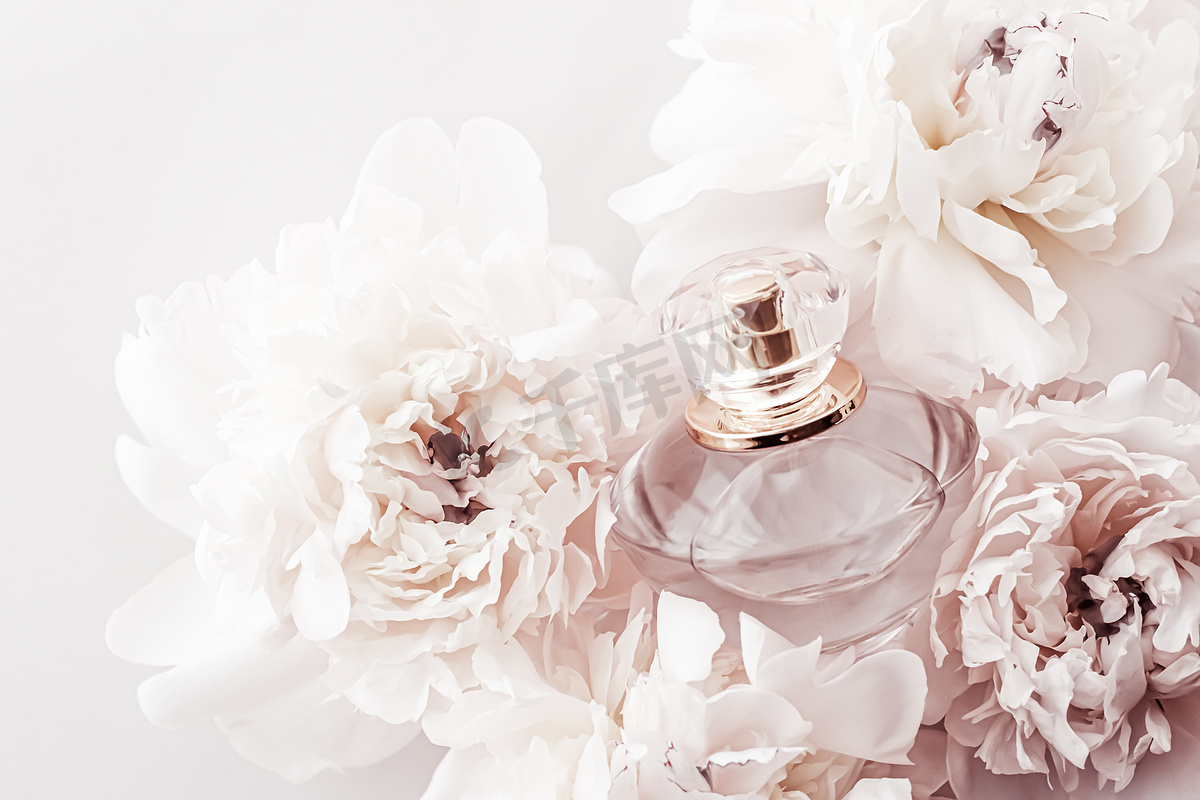 香水瓶作为牡丹花背景下的豪华香水产品、香水广告和美容品牌图片