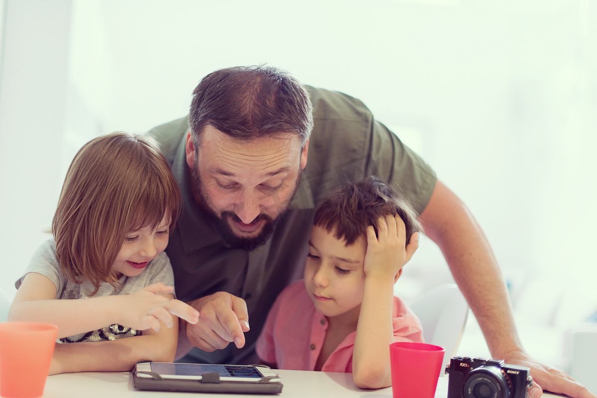 单亲父亲在家带着两个孩子在平板电脑上玩游戏图片