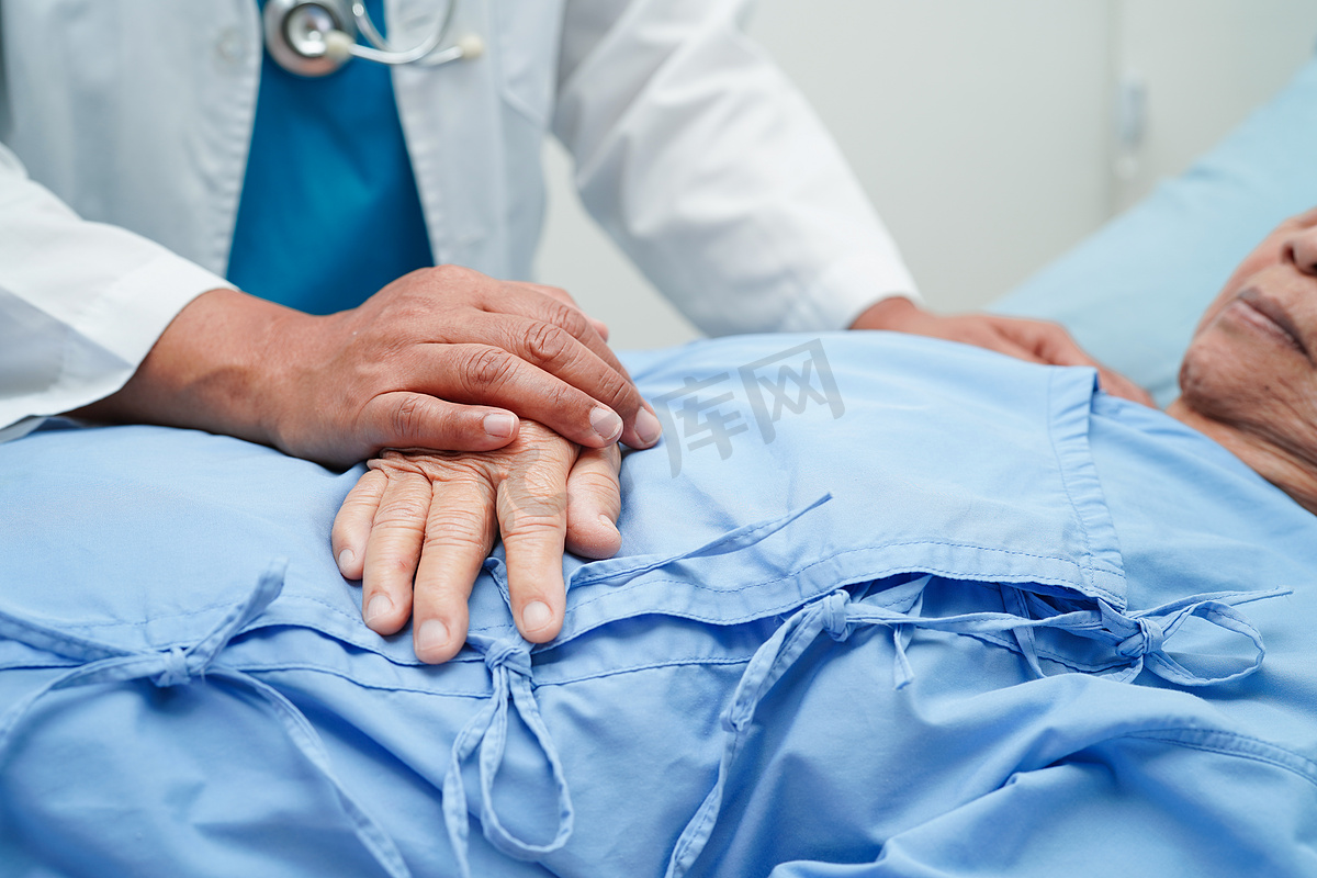医生手牵亚洲老年女病人的手，在医院提供帮助和护理。图片