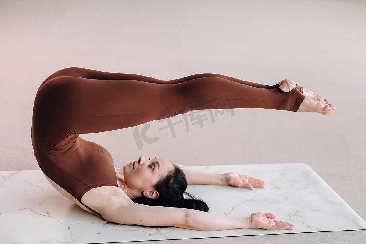 一位身穿棕色西装的女士在健身房里做瑜伽。图片