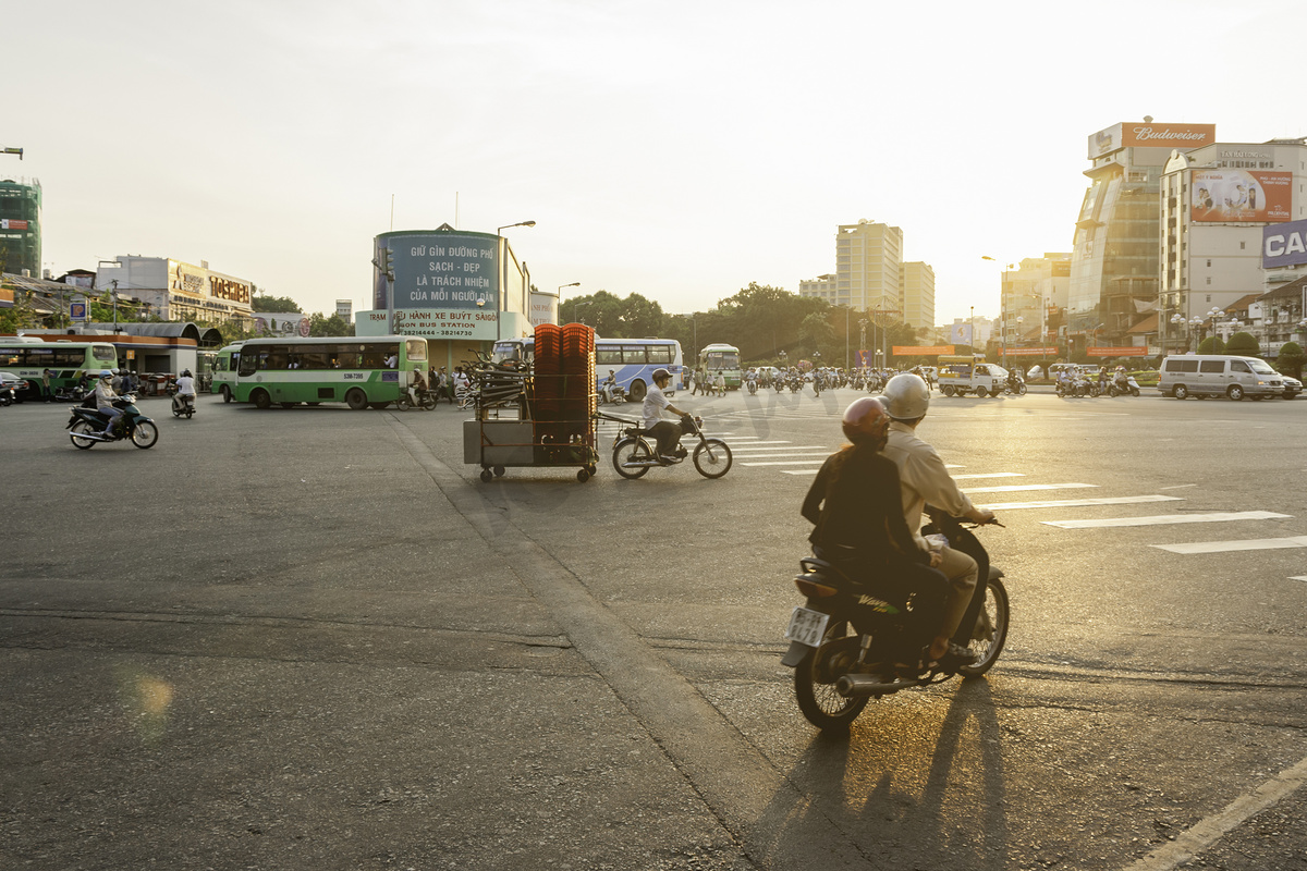 越南胡志明市 - 2009 年 3 月 28 日。日落时分，一名男子在拖车上驾驶着带有桌子和凳子的摩托车沿着首都街道行驶。图片