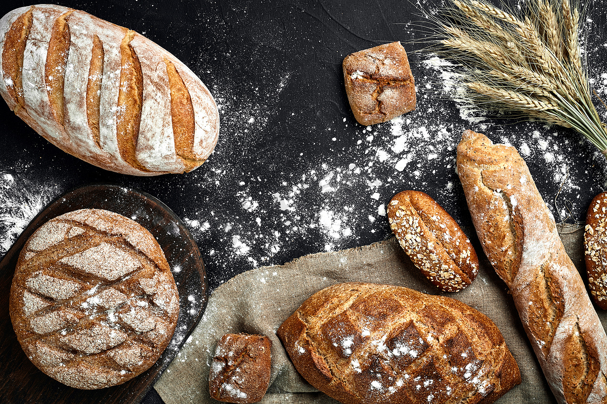 法式长棍面包、烤面包、面粉和小麦穗组合物的顶视图，深色背景上撒有小麦粉图片