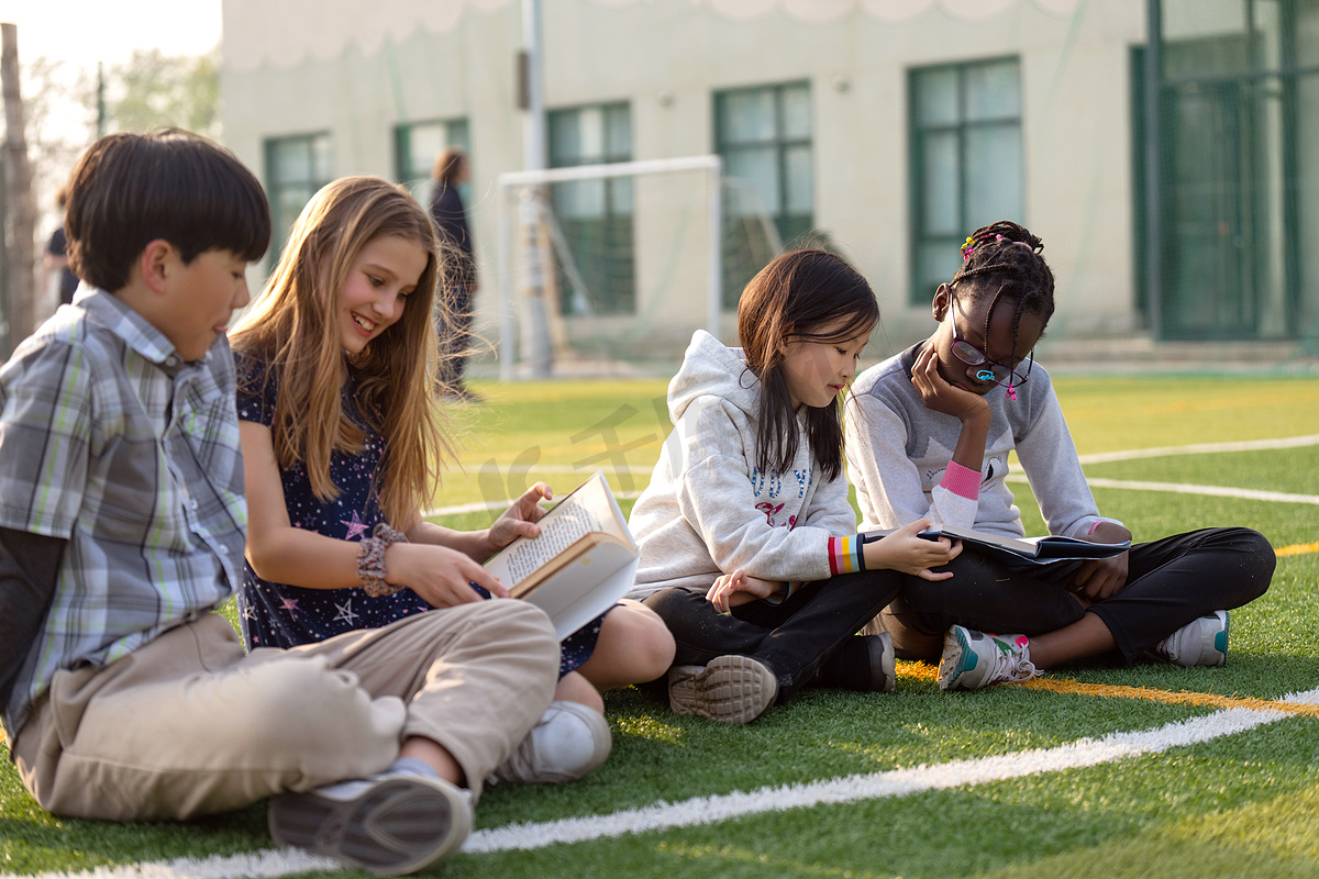 国际学校学生坐在草地上看书图片