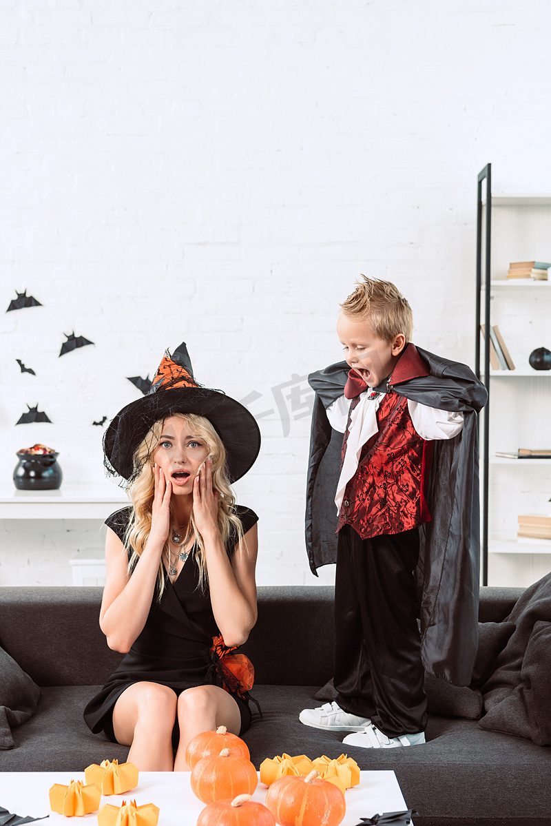小男孩在吸血鬼服装在母亲尖叫在女巫万圣节服装在家里图片
