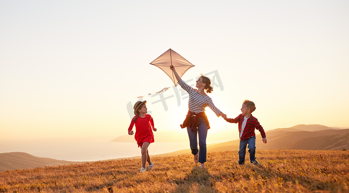 快乐的家庭母亲和孩子们在日落时分放风筝图片