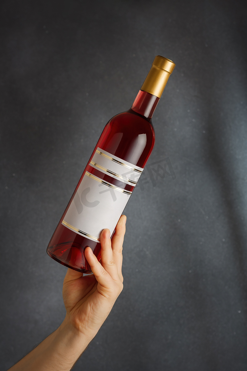 男性手握瓶装粉红色红酒，天然果酒，带有空白标签的灰色背景。造型，品牌模板，垂直拍摄图片