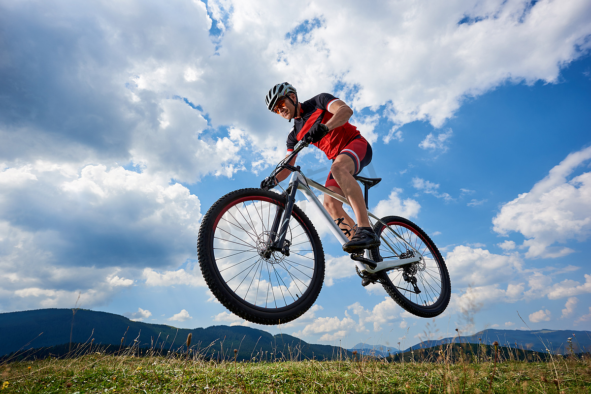 运动运动员骑自行车在专业运动衫和头盔跳跃骑脚踏车与天空和遥远的山在背景下, 户外极限运动概念 图片