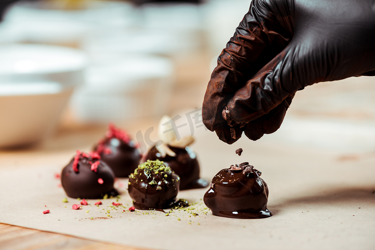用黑色乳胶手套在新制作的糖果上加巧克力屑的巧克力粉的剪影 图片
