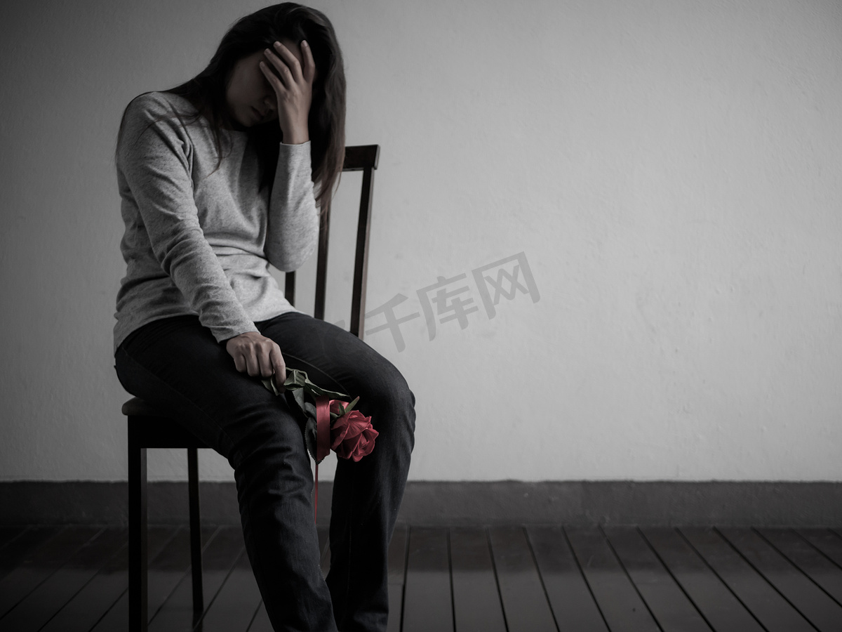 伤心心碎的女人坐着, 哭着红玫瑰独自在黑暗的房间在家. 图片