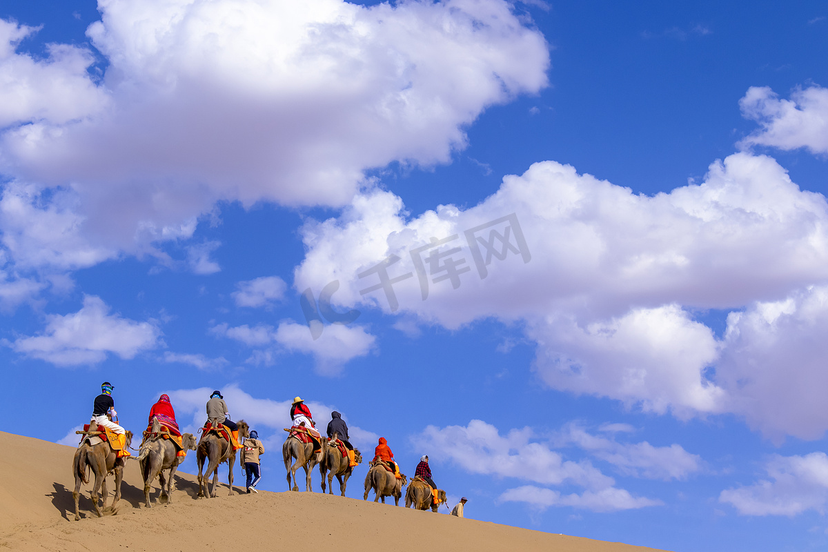 作为中国甘肃敦煌丝绸之路的一部分，成群结队的游客正在明沙山沙漠骑骆驼，或与商队一起在沙丘歌唱.图片