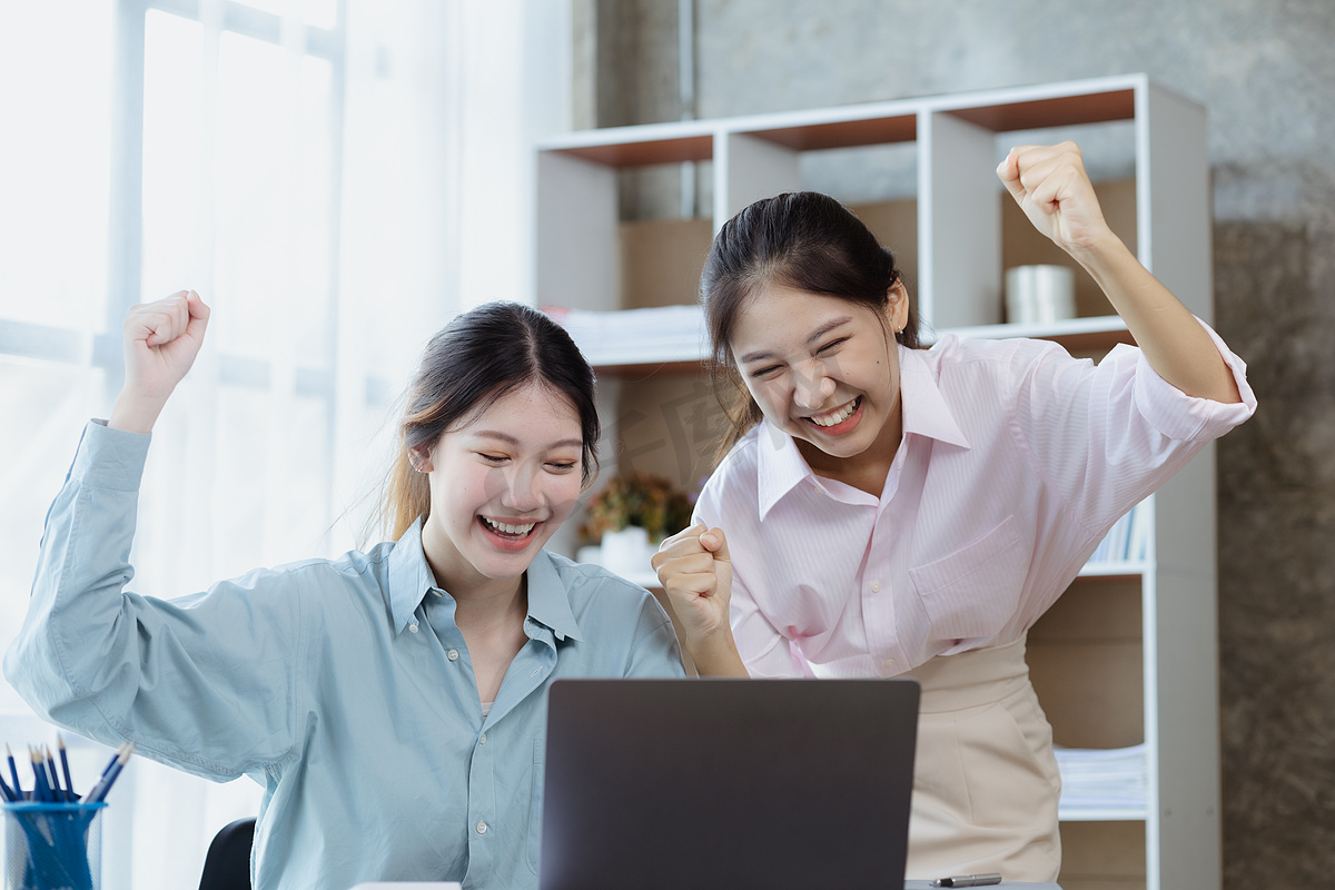 两名女性在笔记本电脑上显示出喜悦和数据，两名商业女性在每月的销售情况总结中超越了销售目标，实现了盈利增长。销售管理概念图片